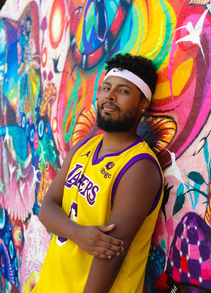 Man in colorful environment wearing a Lakers jersey, posing confidently with a vibrant mural background.