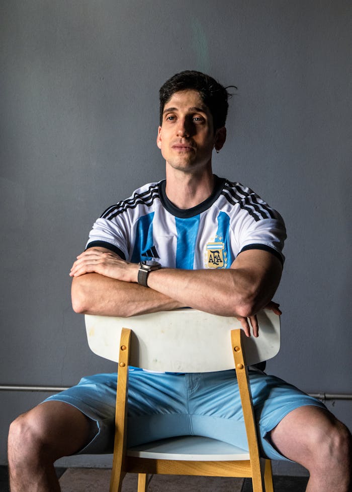 Man sitting on a chair wearing an Argentina football jersey, arms crossed.